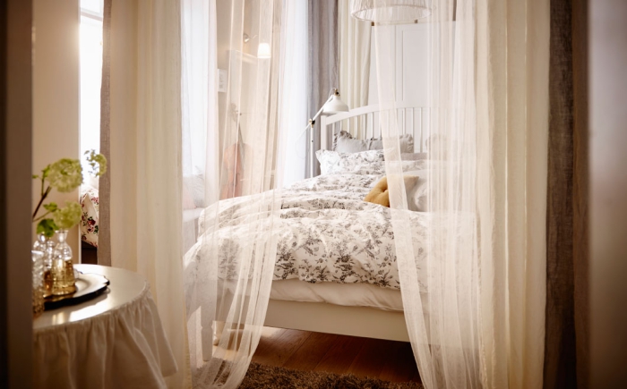 ambiance romantique dans la chambre à coucher avec voiles beige et lit de cadre bois blanc, déco du plancher en bois avec tapis moelleux en marron