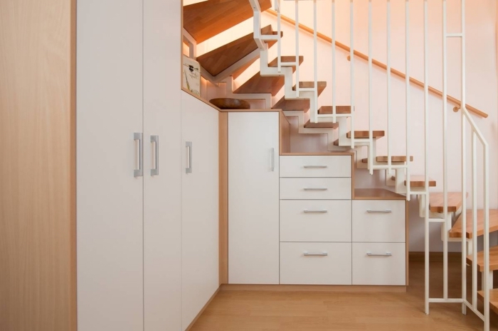 aménagement sous escalier avec garde-robe et armoires d'angle en bois et portes blanches