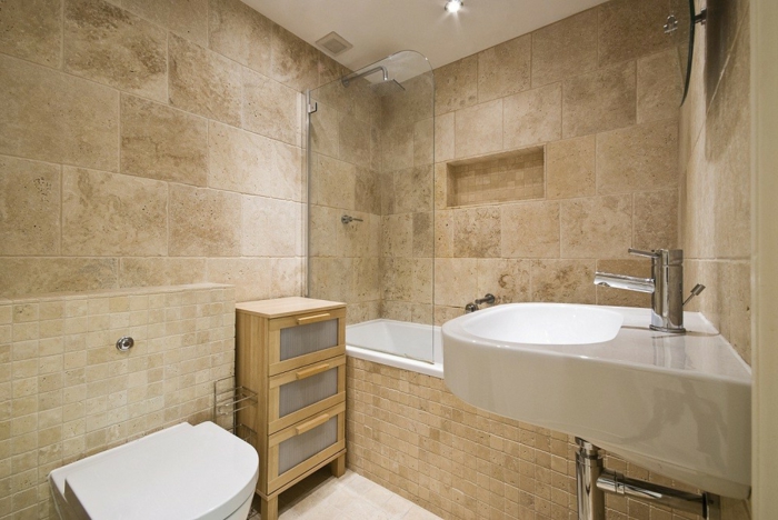 salle de bain en pierre, vasque suspendue blanche, plafond blanc, placard en bois