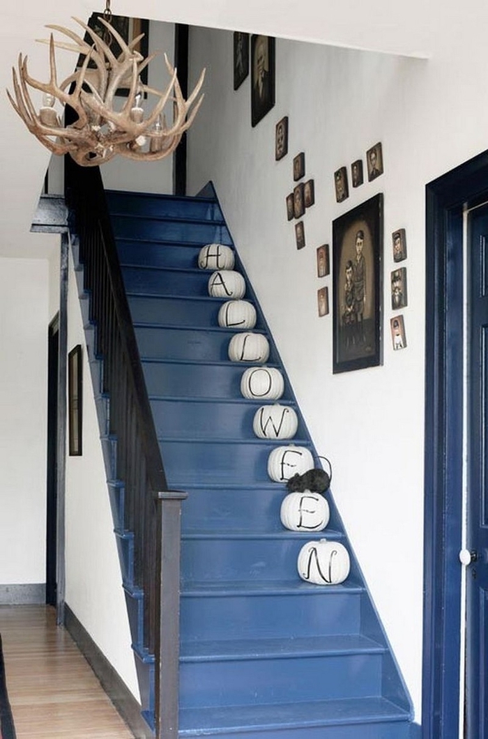 deco montee escalier pour la fête d'halloween avec des citrouilles repeintes à chaque marche, escalier peint en bleu en contraste avec les murs blancs