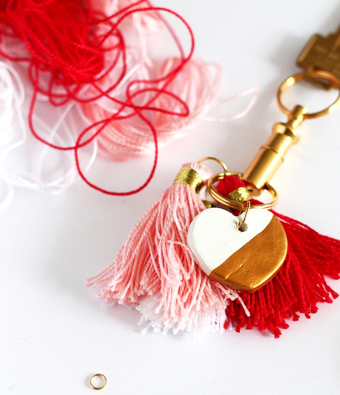 exemple de diy porte clé couleur dorée avec pompons à franges rose et rouge et petit coeur en pate fimo blanc et or