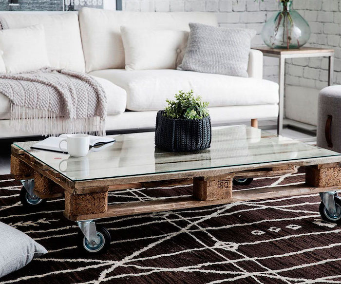 table basse palette de vois, façon rustique avec plateau en verre et des roulettes, canapé blanc cassé, tapis marron