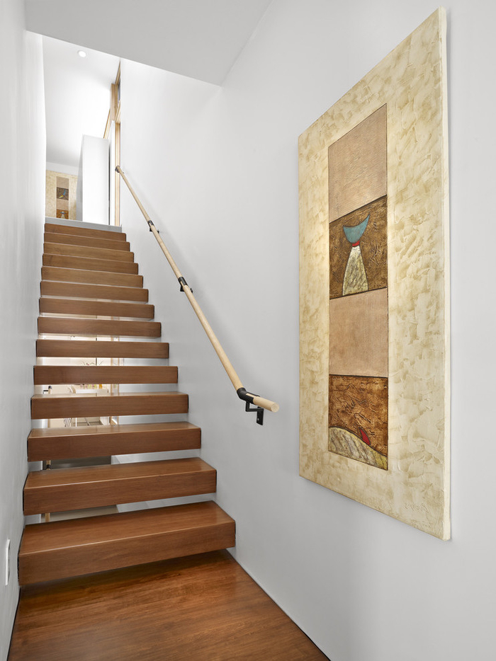 cage d'escalier au design minimaliste décoré d'un grand tableau en tons chauds qui s'harmonise avec l'escalier en bois
