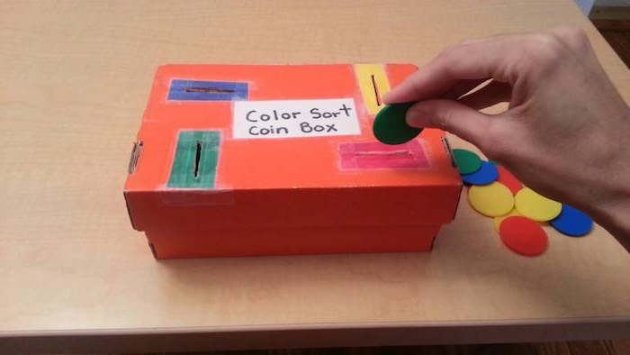 jeu pédagogie montessori en crèche pour apprendre les couleurs, insérer des monnaies colorées dans les fentes correspondantes d une boite en carton, montessori materiel diy