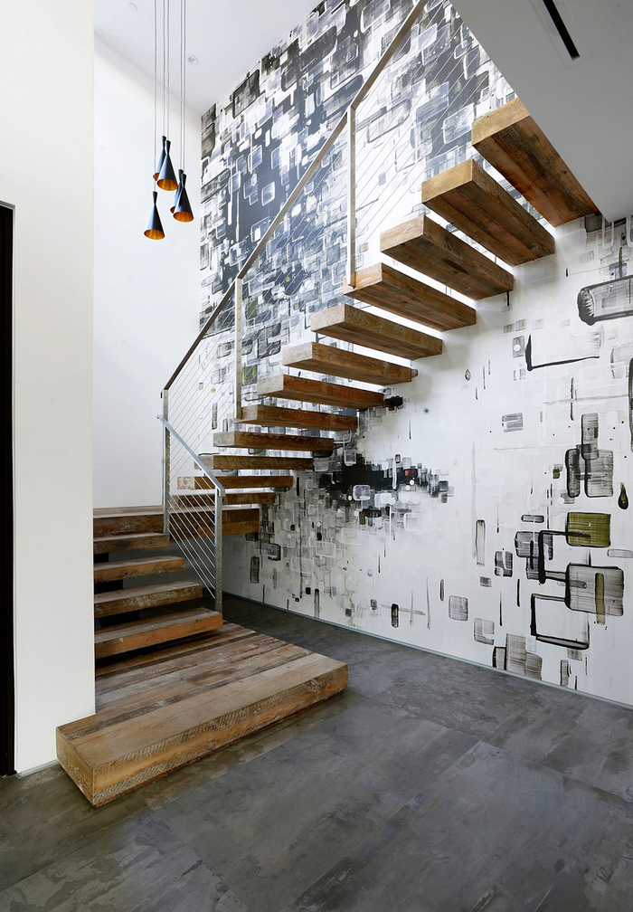 une cage d'escalier de style industriel au mur revêtu de papier peint graphique qui fait ressortir les marches en bois 