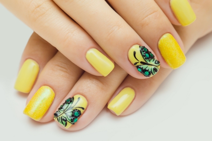 idée manucure pour ongles mi-longs de couleur jaune avec dessin sur l'annulaire à design papillon vert avec strass noirs