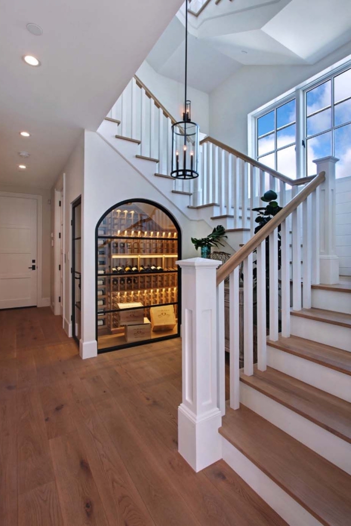 rangement sous escalier en verre pour stocker les bouteille de vin, design intérieur dans le couloir blanc avec parquet de bois
