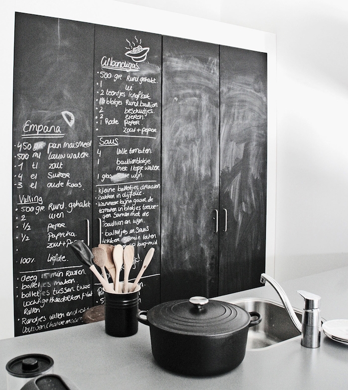 exemple de cuisine equipée avec portes armoire en ardoise murale avec des recettes écrites à la craie et ustensiles de cuisine noires