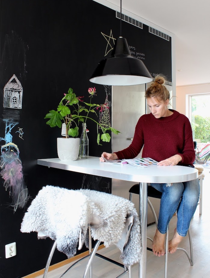 peinture ardoise sur un mur dans la cuisine, petite table ilot inox, chaise avec jeté scandinave, dessins enfan, suspension noire