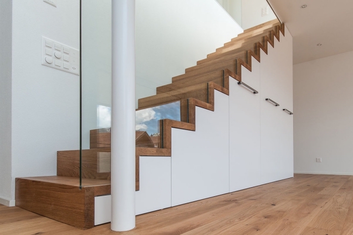 rangement sous escalier blanc avec poignées métalliques, couloir aux murs blancs et plancher de bois clair