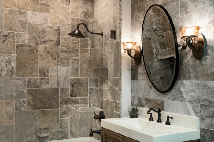 miroir rond au mur, vasque blanche, deux appliques murales, petit espace de douche, pierre travertin