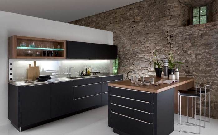 cuisine moderne aux armoires noires matte avec mur blanc et mur en pierres, éclairage led sous meubles de cuisine