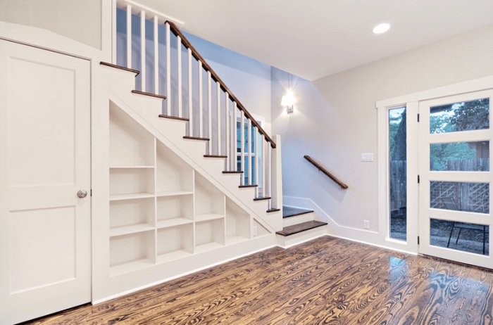 aménagement sous escalier avec étagères blanches en bois et porte, déco intérieur aux murs blancs et plancher de bois