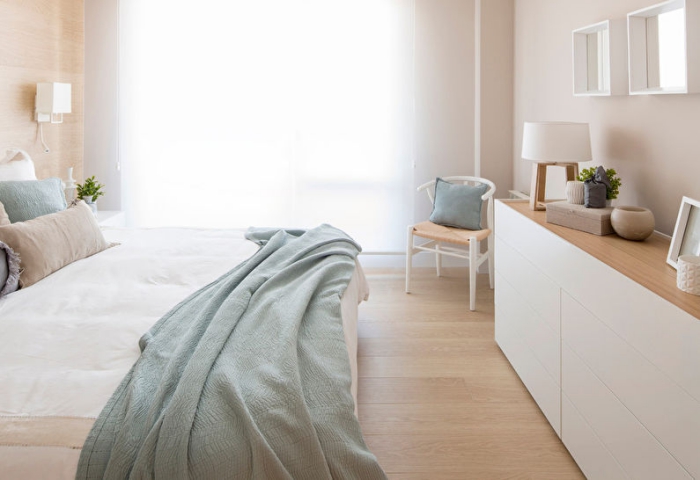 esprit scandinave et minimaliste dans la chambre à coucher aux murs et sol de bois clair avec coussins et plaids de nuance vert pastel