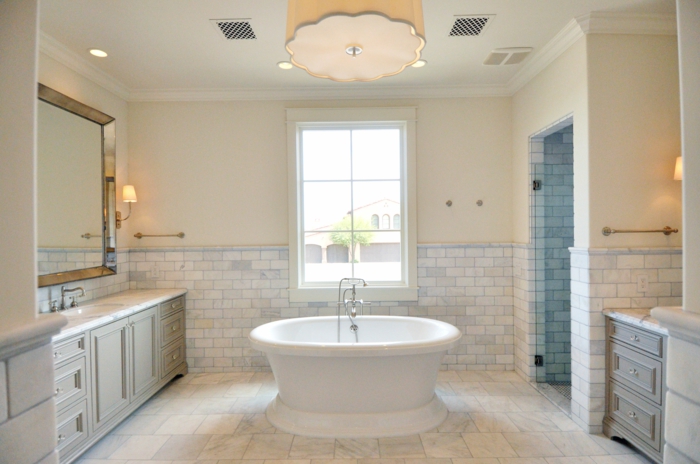 plafonnier beige, baignoire au centre de l'espace, miroir rectangulaire encadré, meubles sous vasque, travertin salle de bain