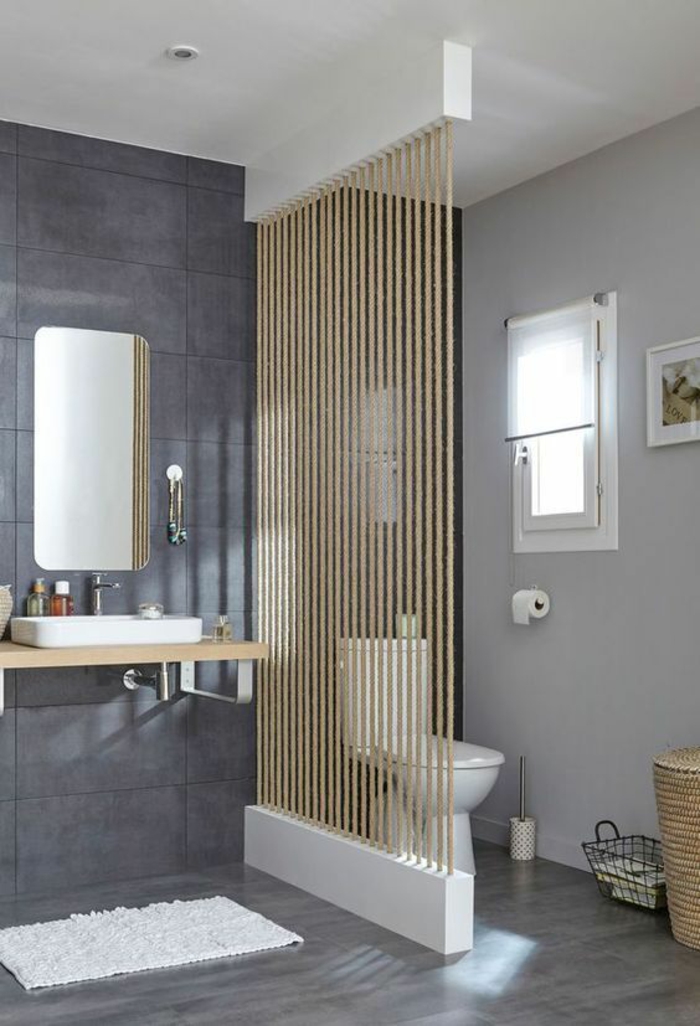 salle de bain 5m2, séparateur d'espace sous forme de fils de laine épais en beige, carrelage gris, mur en gris pastel, miroir rectangulaire au mur, meuble lavabo suspendu, lavabo rectangulaire blanc, tapis rectangulaire en blanc avec effet peluche