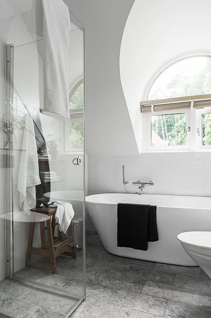 salle de bain 6m2, baignoire ovale blanche- meuble wc blanc, douche italienne en verre transparent, carrelage du sol en gris nuancé, fenêtre semi-ronde 