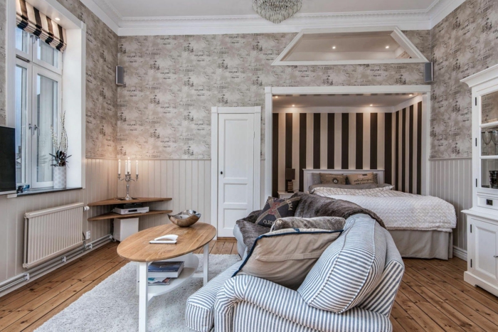 alcôve pour le lit, petite table en bois ovale, sofa à rayures, tapis gris, sol en bois, plafond blanc