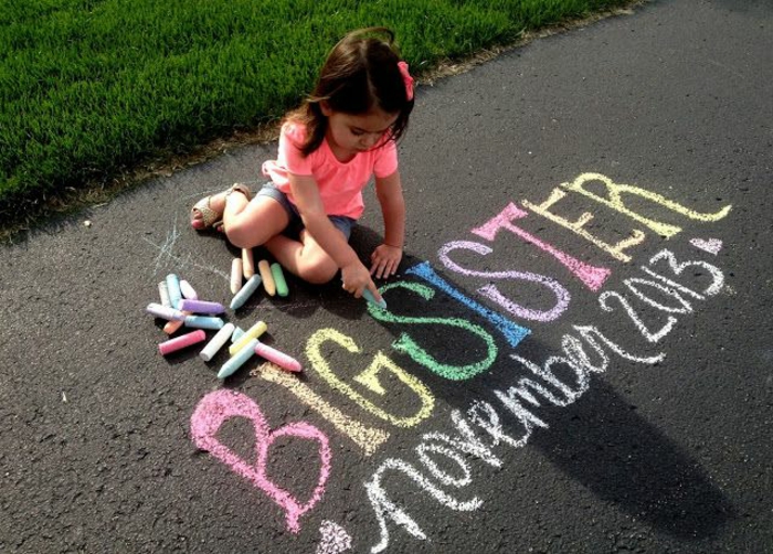 petite fille qui écrit sur l'asphalte, annoncer grossesse en écrivant avec des craies