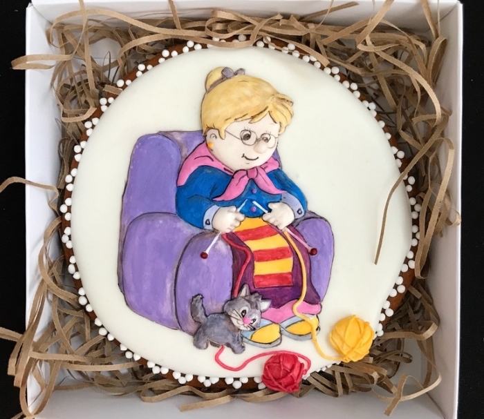 présent délicieux avec un gâteau personnalisé à design mamie aux cheveux blonds assise sur un fauteuil violet avec chien et boules de laines
