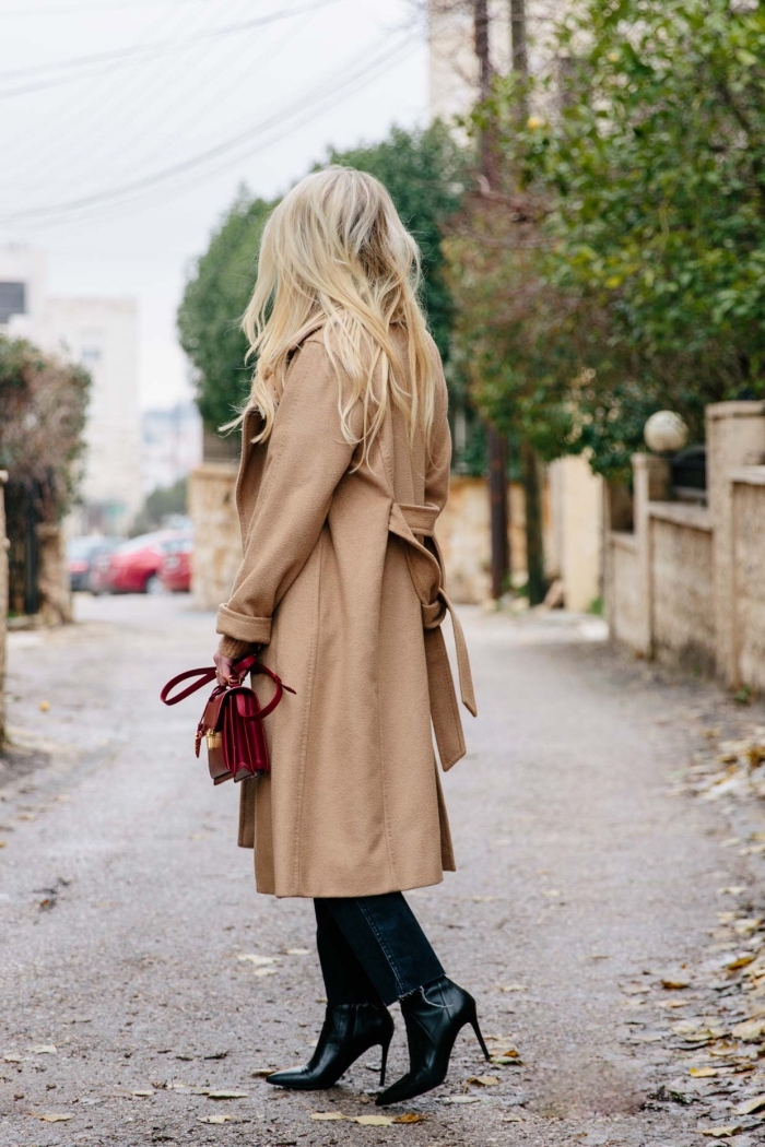 look femme stylée en manteau long camel et bottines en cuir noir à talons hautes, modèle de sac à main couleur bordeaux