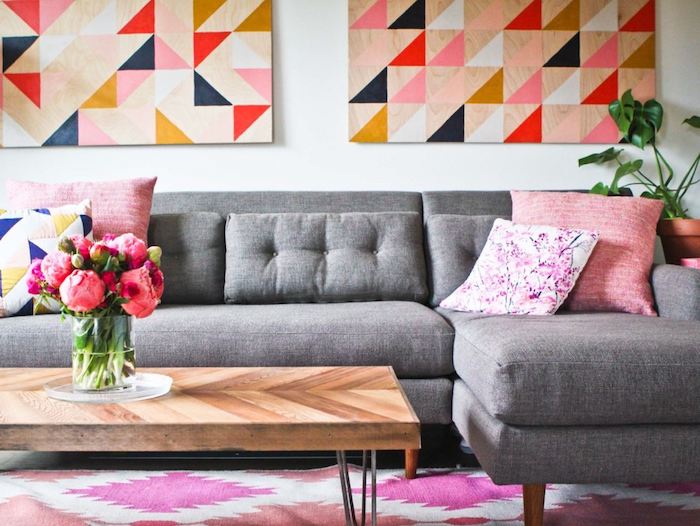avec quelle couleur associer le gris, exemple de canapé d angle gris, coussins décoratifs rose, fleuri et à motifs géométriques, tapis rose et blanc, tableau décoratifs à figures géométriques, table en bois et métal, bouquet de fleurs