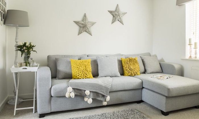 modele de canapé gris clair, coussins gris et jaune, tapis gris, mur blanc décoré d étoiles grises, table en plateau de service