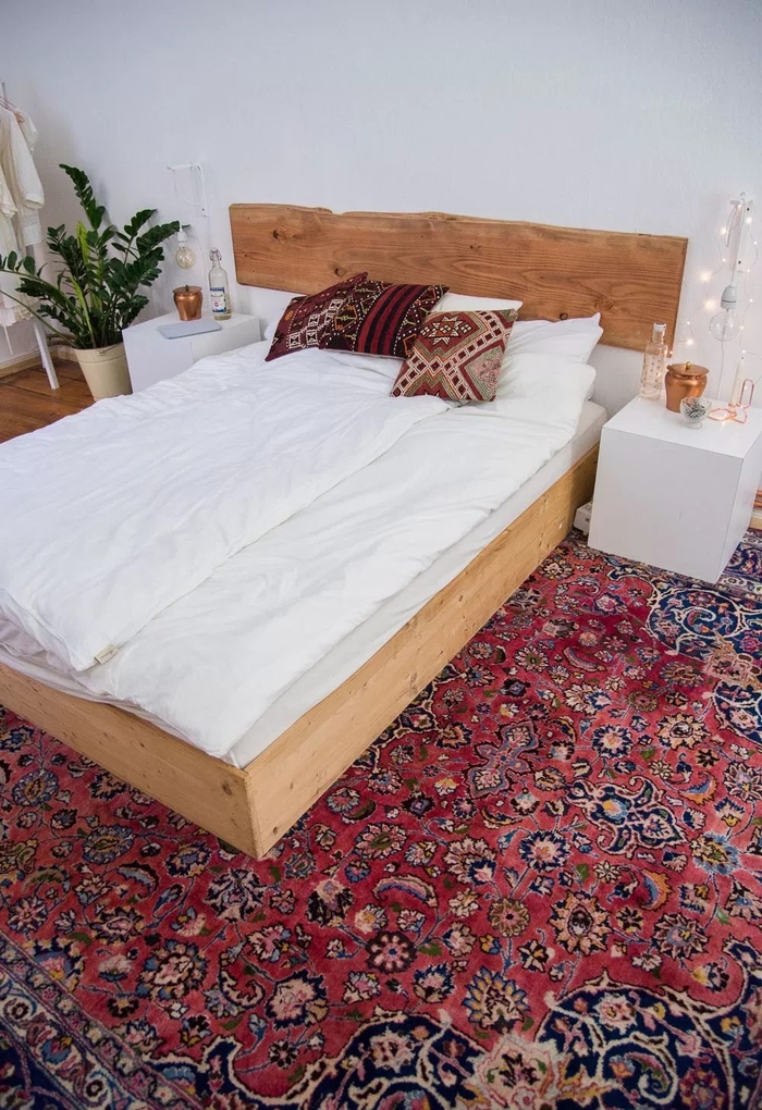 ambiance bohème chic dans la chambre à coucher avec un tapis persan, des coussins qui reprennent ses motif et une tete de lit bois brut