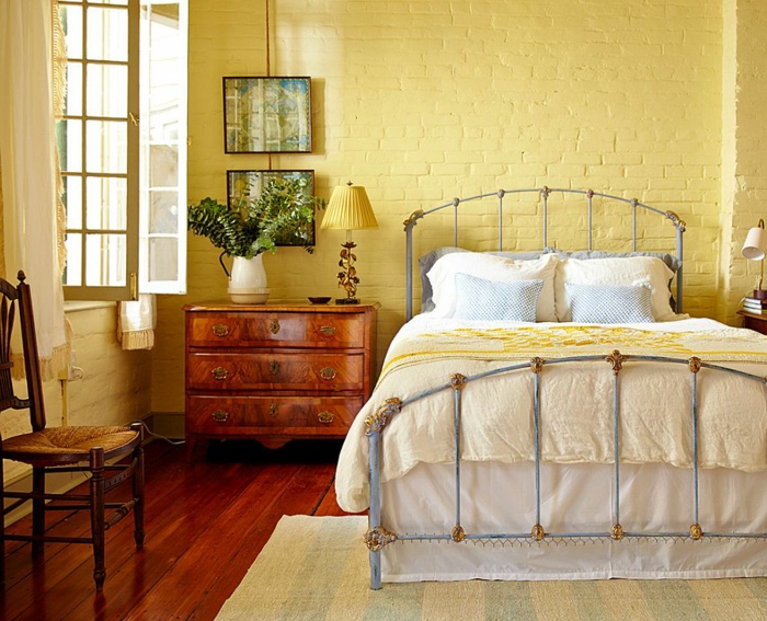 plancher en bois, lit vintage, mur en briques apparentes peintes jaunes, chaise rétro