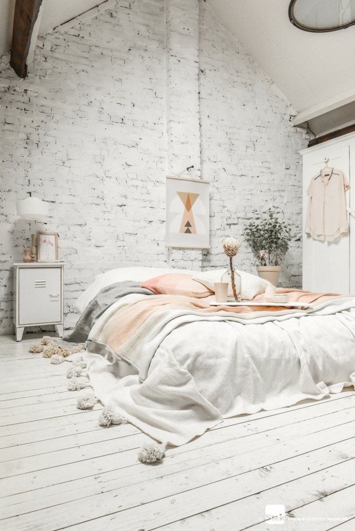 lit bas, linge de lit pompons, mur en briques, sol en planches blanches, intérieur tout blanc
