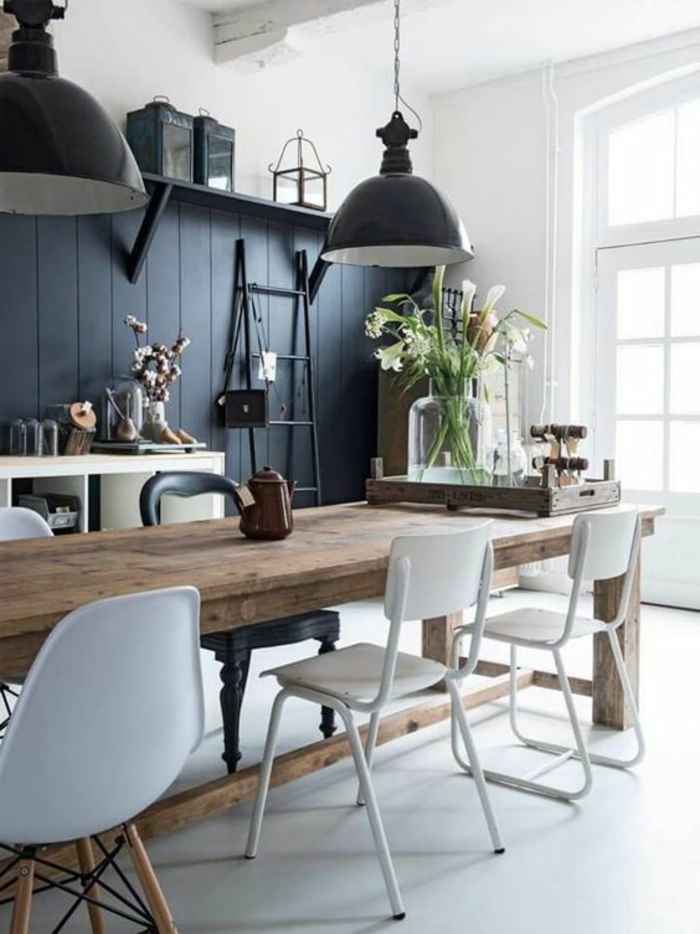 un mur en gris anthracite, des nuances de gris pour repeindre sa cuisine, deux grands luminaires en métal noir, chaises blanches et noires, en plastique et en métal, sol blanc, grande table rectangulaire en style rustique