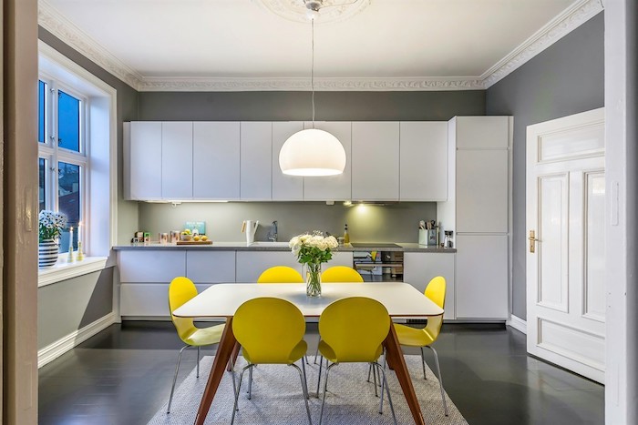 mur repeint de peinture grise, meuble de cuisine gris, suspension blanche, sol gris et ouverture sur salle à manger en chaises jaunes et table blanche
