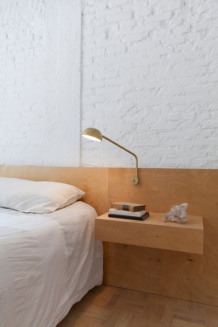 ambiance monochrome et épurée dans une chambre à coucher qui joue sur le contraste des murs en briques blanches et la tete de lit bois