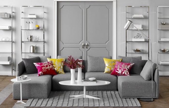 murs décorés de peinture gris clair, canapé gris, coussins framboise et jaunes, parquet marron, etageres metalliques, table basse blanche