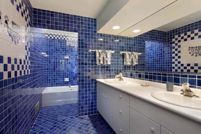 carrelage blanc et bleu foncé dans une salle de bain moderne avec éclairage led et meubles blancs, baignoire blanche et carrelage bleu marine