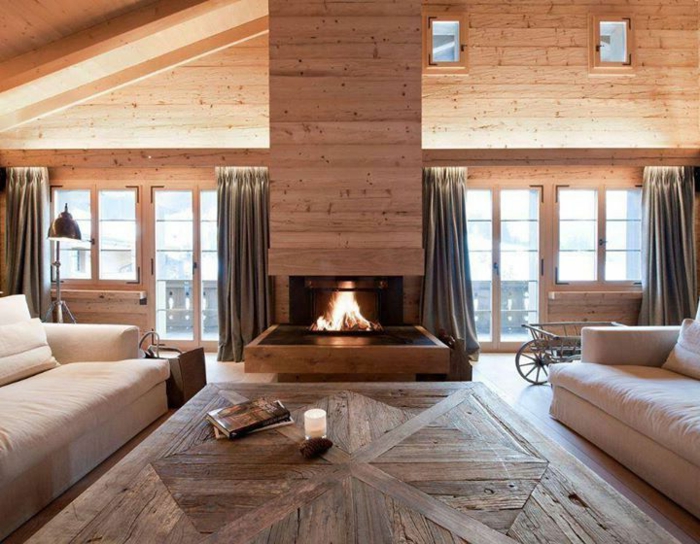 deux grands sofas beiges, sol en bois, cheminée, intérieur style chalet, fenêtres du plafond au sol