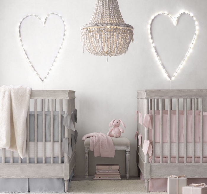 chambre bébé fille ou garçon aux murs blancs avec décoration lumineuse et deux lit à barreaux de bois gris avec linge gris et rose pastel