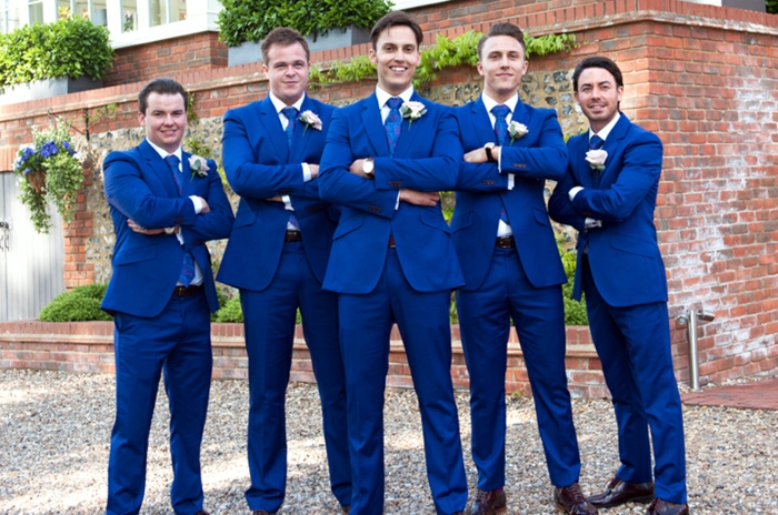 cinq témoins de mariage en costume bleu roi, avec des revers ornés de fleurs blanches, ambiance de château, chaussures en marron foncé 