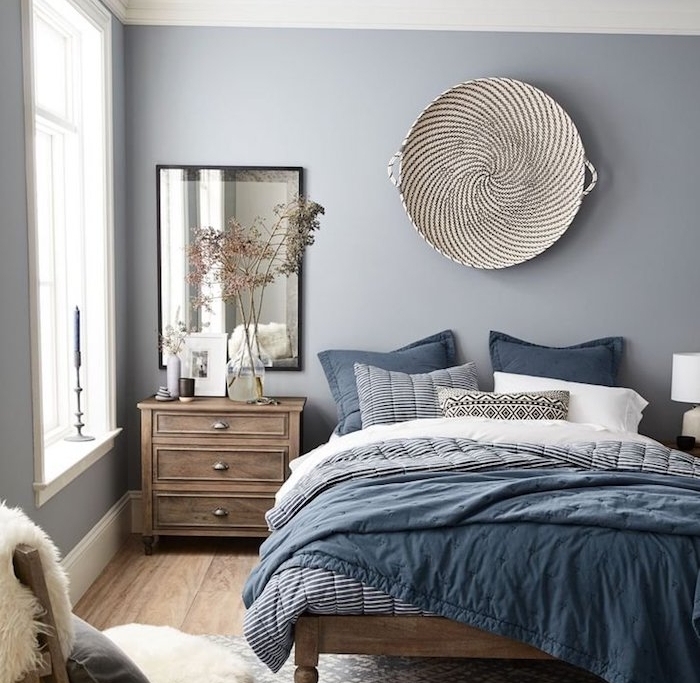mur couleur peinture gris perle, linge de lit blanc, bleu et noir, lit et table de nuit bois foncé, parquet clair, panier en déco murale