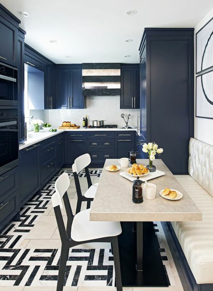 comment moderniser une cuisine en chene, repeindre meuble cuisine en bleu canard, sol en dalles noir et blanc aux motifs graphiques, table rectangulaire en beige, canapé en couleur ivoire, deux chaises en blanc et noir
