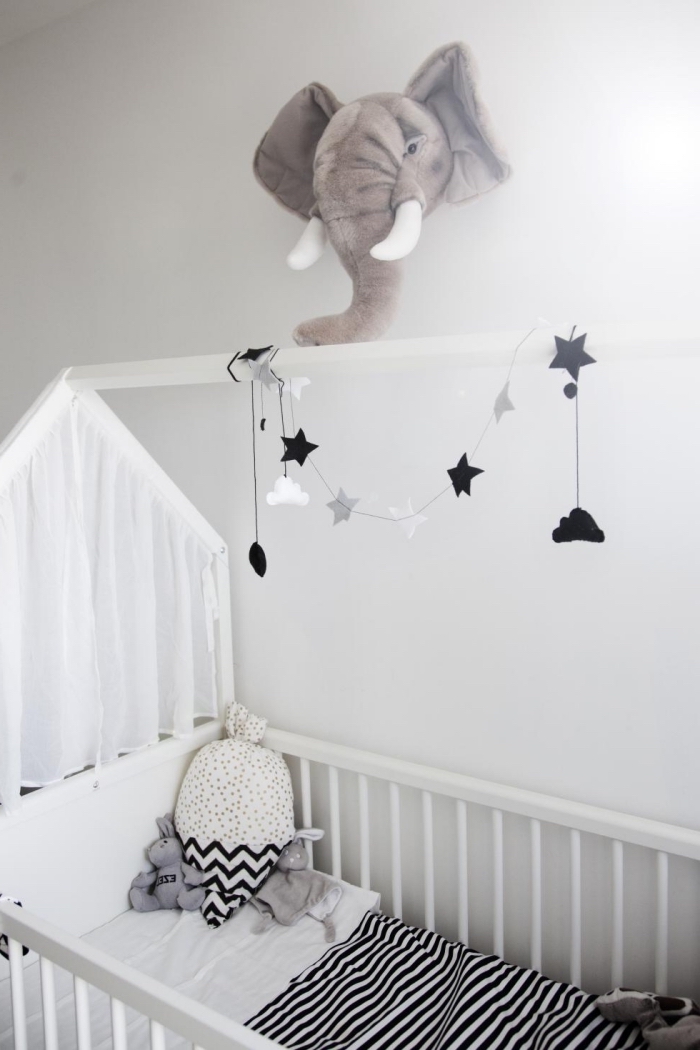 aménagement de la chambre bebe blanche avec lit à barreaux de bois blanc et décoration murale en forme de tête éléphant en péluche