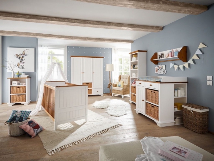 chambre bébé en style campagne avec murs peints en bleu clair et meubles blanc et bois, modèle de tapis beige avec frange sur un plancher de bois clair
