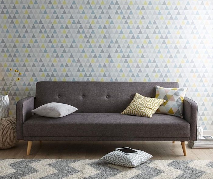 canapé nuance gris anthracite, mur habillé de papier peint à triangles blancs, gris et jaunes, tapis gris et blanc