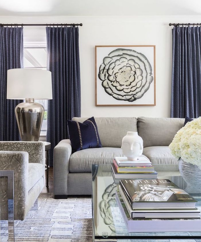 amenagement salon moderne avec canapé gris clair, rideaux bleu foncé, table basse en verre et fauteuil gris