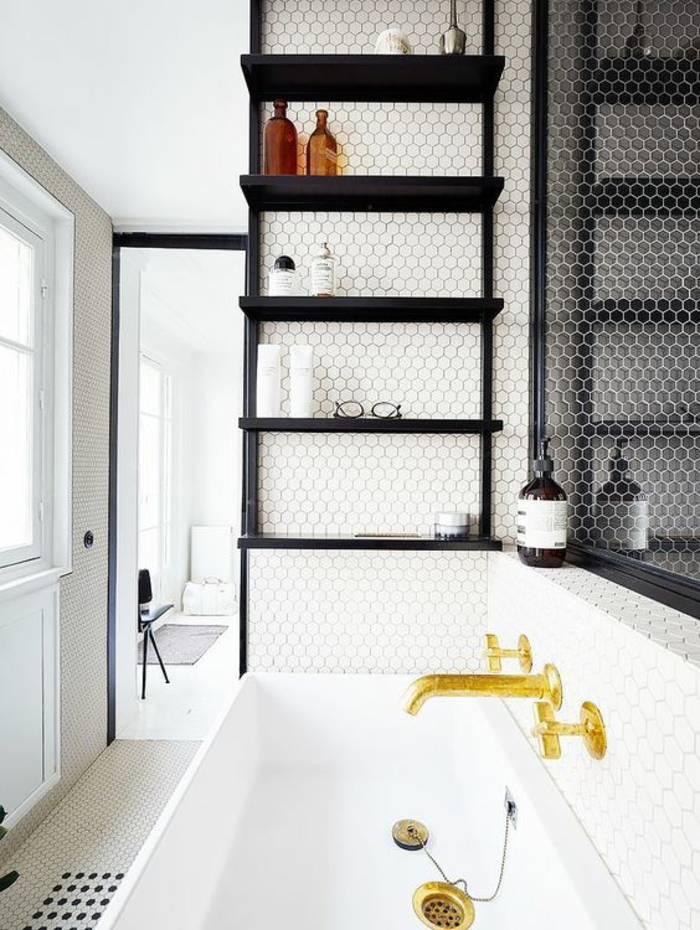 murs avec carrelage hexagonal en noir et blanc, salle de bain 6m2, baignoire en blanc avec des robinets en couleur or, étagères noires au-dessus de la baignoire, solution pour optimiser au max l'espace 
