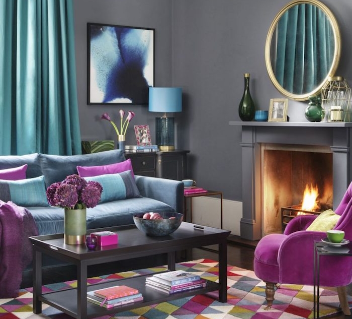 murs peinture gris anthracite avec cheminée design, rideaux et canapé bleu, table basse marron foncé, coussins et fauteuil fuchsia, tapis à triangles colorés