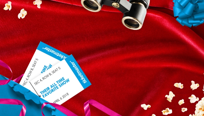 billets de spectacle sur une nappe rouge couverte de popcorns, modèle de binocles et emballage de cadeau en papier bleu