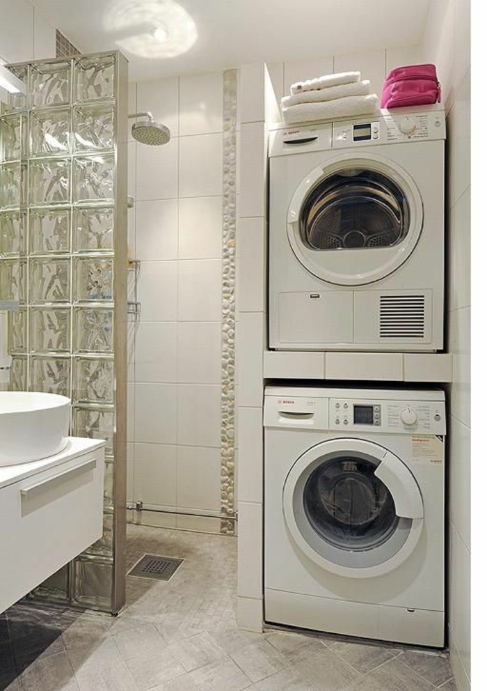 salle de bain 6m2, lave-linge et sèche-linge installés l'un au-dessus de l'autre, grande douche séparée du reste du bain avec une verrière épaisse arty, meuble lavabo suspendu en blanc, carrelage en gris 
