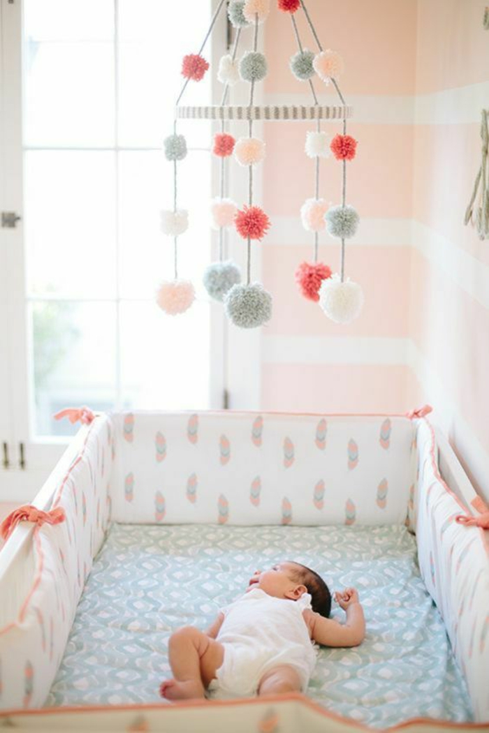 chambre rose et gris, décoration chambre bébé fille, matelas recouvert de drap en couleur pastel, des pompons multicolores suspendus au-dessus du lit, murs en couleur saumon et blanc