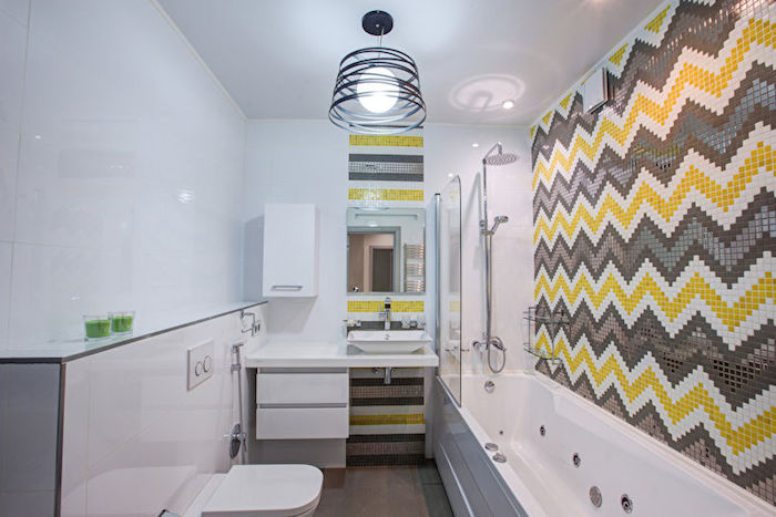 idée d agencement salle de bain en longueur, mur en carrelage gris, blanc et jaune, petite baignoire, parquet marron foncé, toilette suspendu, lustre original